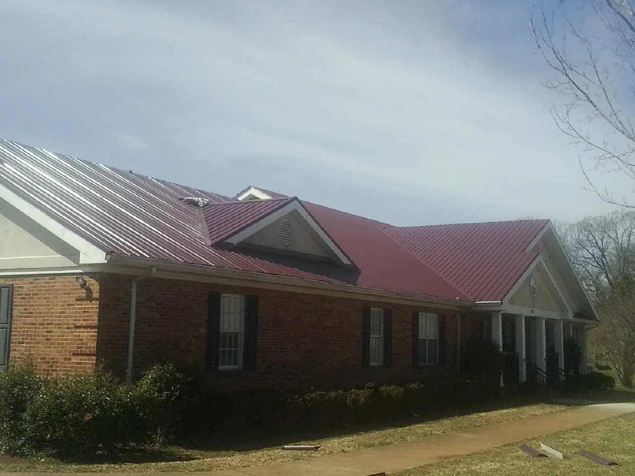 Red metal roof with gabled entries on a long brick building, from a Hail Damage Roof Repair job in Klingerstown