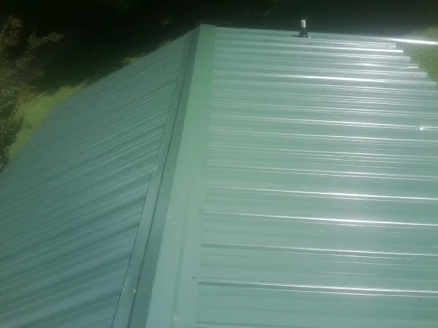 New green metal panels meeting at the ridge of a roof — Flat Roof Repair work by our crew in Klingerstown
