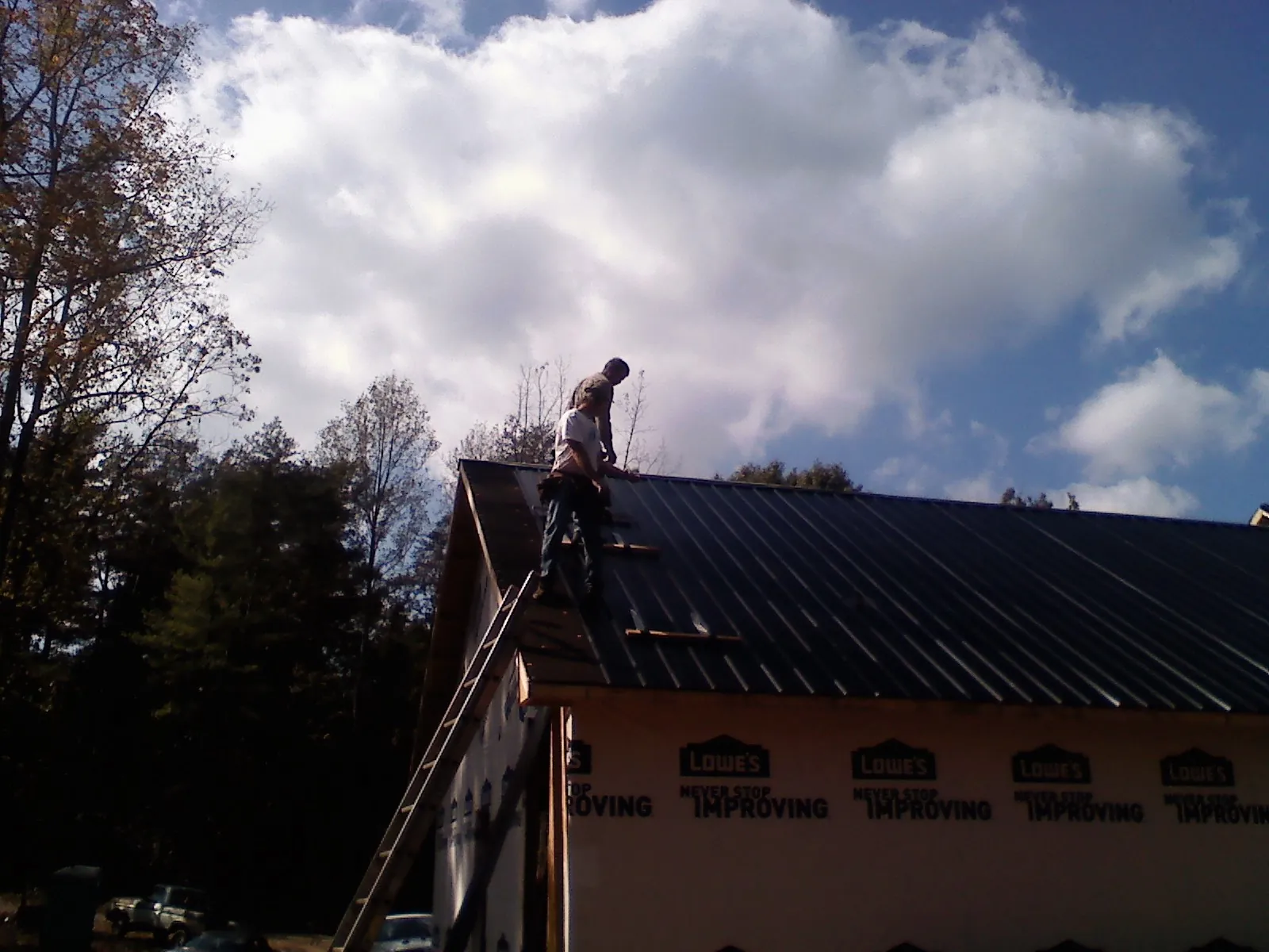 Roofer fastening dark metal panels high against a cloudy sky, from a Roof Inspection job in Klingerstown