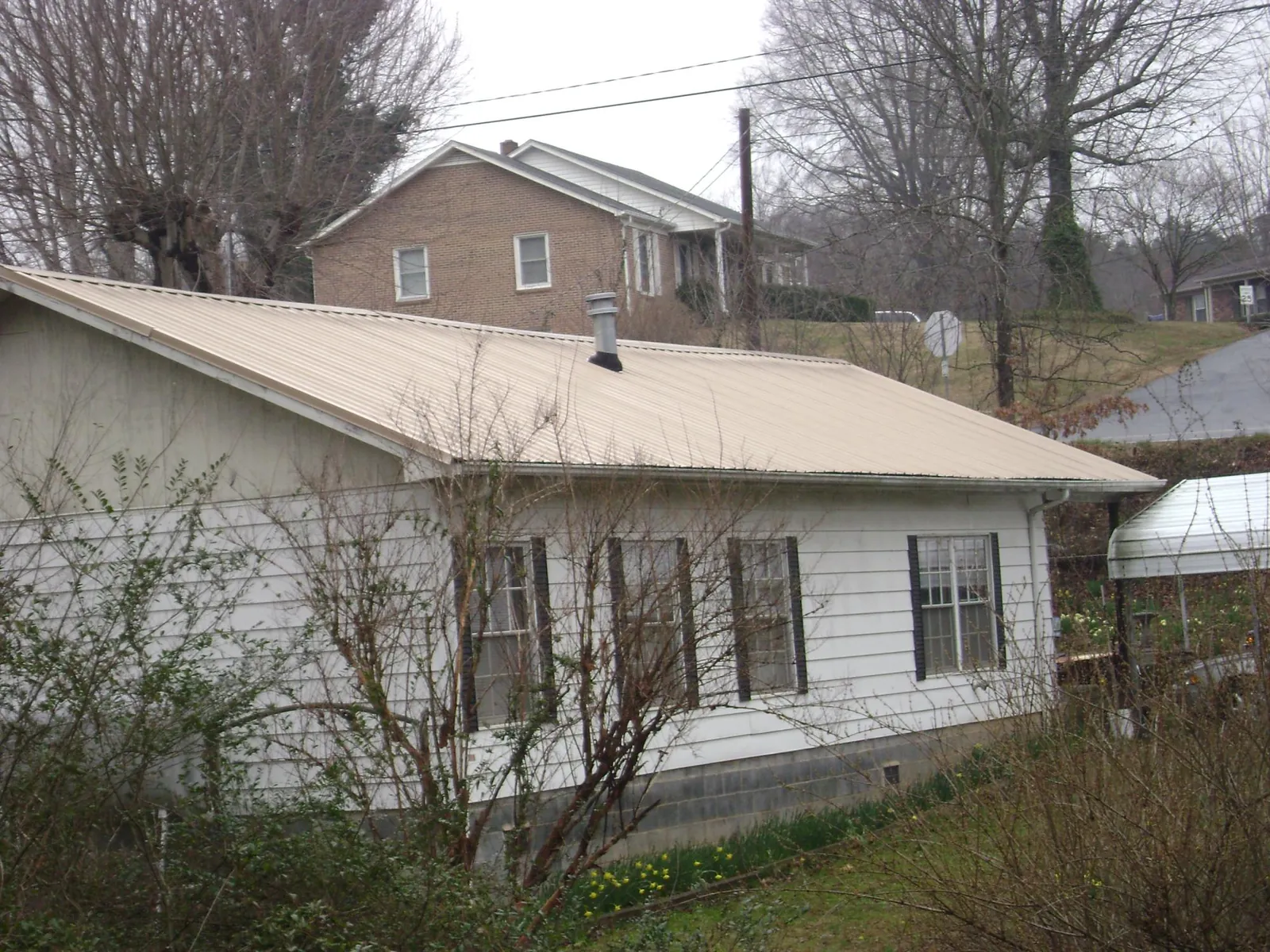 Tan metal roof on a white sided house set into a hillside — Commercial Roofing by Roofing Brothers in Klingerstown